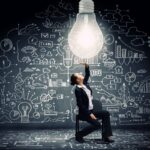 Young businesswoman sitting on chair with big light bulb above